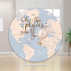 Könnte beinhalten: Ein runder Hintergrund mit einer Weltkarte in gedämpften Blau- und Beigetönen. Der Text "Oh the places you'll go" ist in brauner Schrift geschrieben. Eine Heißluftballon-Illustration ist ebenfalls vorhanden. Der Hintergrund wird von einem weißen Metallständer getragen.