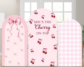 May include: Three pink arched backdrop panels. One features a large bow and small bows, another has cherries and the text "She's the Cherry on Top", and the third has a pink gingham pattern. The panels are on silver stands.