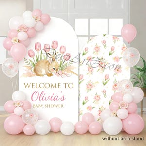 May include: A baby shower backdrop with pink and white balloons, floral accents, and a bunny illustration. The sign reads "Welcome to Olivia's Baby Shower."