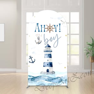 May include: A white backdrop with a nautical theme, featuring a lighthouse, anchors, and the text "Ahoy! It's a boy." The design incorporates watercolor waves and a ship's wheel in shades of blue and brown. The backdrop is supported by a metal frame.
