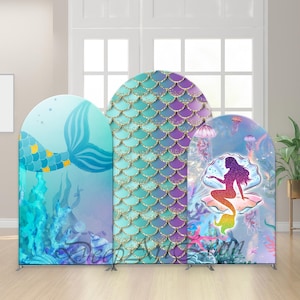 Puede incluir: Tres paneles de fondo con temática de sirenas. Los paneles presentan colas de sirena, patrones de escamas y una silueta de sirena en una concha. Los colores incluyen turquesa, morado y dorado. Los paneles tienen forma de arco en la parte superior y se apoyan en marcos metálicos.