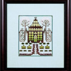 May include: Cross-stitch artwork of a detailed building with a green roof and windows, framed by trees and decorative gates. The artwork features a symmetrical design with a pathway leading to the building, all within a dark wooden frame.
