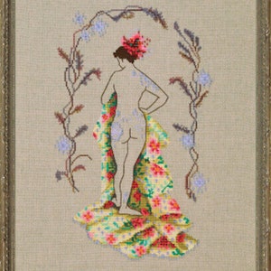 May include: Cross-stitch artwork of a figure with floral accents, framed in a silver-colored frame. The figure is seen from the back, adorned with a floral headdress and a patterned wrap. A floral arch frames the figure, adding a decorative touch.