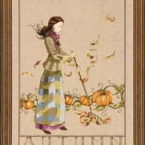 Può includere: Opera d'arte a punto croce in una cornice dorata raffigurante una donna che rastrella le foglie vicino alle zucche. Indossa una gonna a quadri verdi e blu, una sciarpa viola e una giacca color cachi. La parola "AUTUMN" è ricamata in basso.