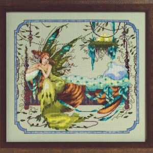 Puede incluir: Obra de arte de punto de cruz de un hada en una cama, enmarcada en un marco de madera. El hada tiene el pelo rojo y alas verdes y azules. La cama está decorada con detalles azules y verdes, y el fondo es verde claro.