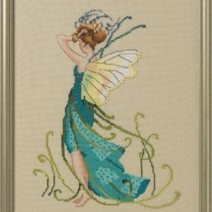 May include: Cross-stitch artwork of a fairy in a teal dress with yellow and white wings. The fairy has red hair and is surrounded by green vines. The artwork is framed in a gold-colored frame.