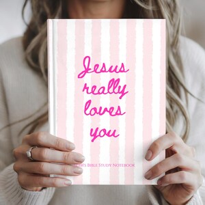 May include: A hardcover notebook featuring a vertical striped pattern in light pink and white. The front cover displays the hot pink text "Jesus really loves you" in a cursive script, with the smaller text "BIBLE STUDY NOTEBOOK" below it.