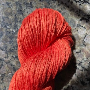 May include: A vibrant orange skein of yarn, tightly wound and textured. The yarn appears to be made of a soft, natural fiber, perfect for knitting or crocheting projects. The color is a bright, warm hue, ideal for various craft creations.