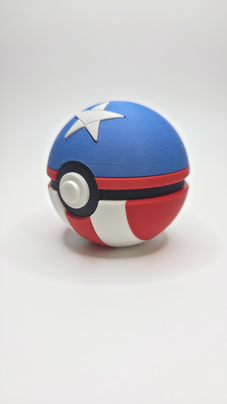Peut inclure: Une Pok&eacute; Ball rouge, blanche et bleue avec une &eacute;toile blanche sur la moiti&eacute; sup&eacute;rieure bleue. La balle a une bande noire et un bouton blanc. Le design rappelle un th&egrave;me patriotique.