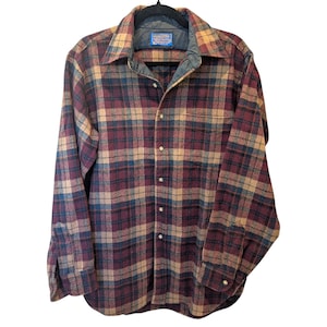 May include: A long-sleeved plaid shirt in shades of burgundy, tan, and blue. The shirt has a button-down front, a collared neckline, and two chest pockets. The shirt is made of a soft, woven fabric.