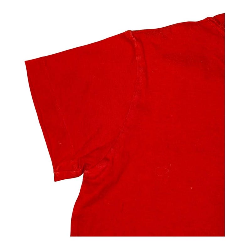 May include: Close-up of a solid red t-shirt, showing the shoulder and sleeve. The fabric appears to be a soft cotton or blend, with a slightly textured surface. The bright red color is consistent throughout the visible portion of the garment.