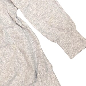 K&ouml;nnte beinhalten: Nahaufnahme eines hellgrauen Sweatshirt-&Auml;rmels und -K&ouml;rpers. Der &Auml;rmel hat ein geripptes B&uuml;ndchen und einen kleinen Fleck. Der Stoff scheint ein weiches, strukturiertes Material zu sein, wahrscheinlich Baumwolle oder eine Baumwollmischung. Das Sweatshirt ist ein Freizeitkleidungsst&uuml;ck.