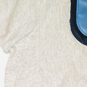 K&ouml;nnte beinhalten: Nahaufnahme eines melierten, kurz&auml;rmeligen Shirts. Das Shirt hat einen hellblauen Aufn&auml;her mit marineblauem Rand auf der rechten Seite. Der Stoff hat ein strukturiertes Aussehen.