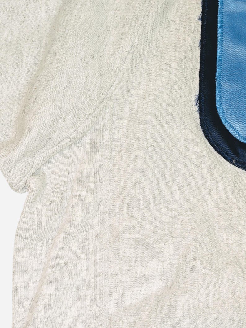K&ouml;nnte beinhalten: Nahaufnahme eines melierten, kurz&auml;rmeligen Shirts. Das Shirt hat einen hellblauen Aufn&auml;her mit marineblauem Rand auf der rechten Seite. Der Stoff hat ein strukturiertes Aussehen.