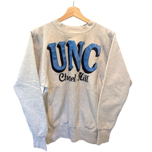 May include: A light gray sweatshirt with the letters "UNC" in light blue with a black outline, and the words "Chapel Hill" in black script. The sweatshirt is hanging on a wooden hanger.
