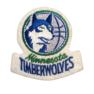May include: Embroidered patch with the Minnesota Timberwolves logo. The patch has a white background with a circular design of a blue and white wolf head and a basketball. The words "Minnesota Timberwolves" are embroidered in green and blue.