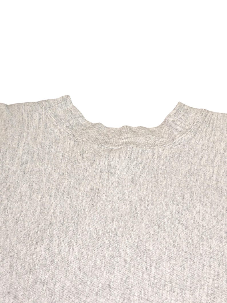 K&ouml;nnte beinhalten: Nahaufnahme eines melierten, grauen Sweatshirts mit Rundhalsausschnitt. Der Stoff hat ein strukturiertes Aussehen. Der Halsausschnitt ist sichtbar und zeigt die gerippten Kragendetails. Der Hintergrund ist schlicht wei&szlig;.