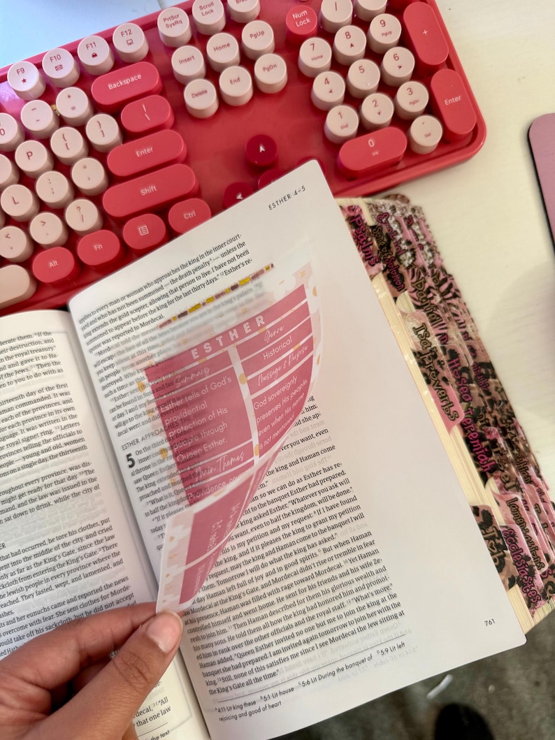 May include: Open book with the text "ESTHER 4-5" and pink tabs. A pink mechanical keyboard is in the background. The book is open to a page with highlighted text and a pink overlay.