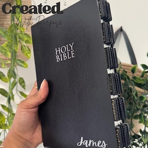 May include: Black Holy Bible with white text and labeled tabs. The cover features the words "HOLY BIBLE" and "James" in white script. The image also includes the text "Created With Purpose" and "Ephesians 2:10".