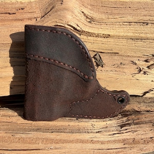 May include: A dark brown leather boot-shaped item with visible stitching. The boot has a suede-like texture on the main body and a smoother leather top. The stitching is a contrasting reddish-brown colour.