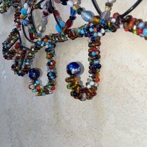 May include: Close-up of a decorative wall hanging with a black metal frame. The design features intricate loops and curves adorned with colourful beads in various sizes and hues, including blue, red, orange, and white. Two blue spherical accents are also present.
