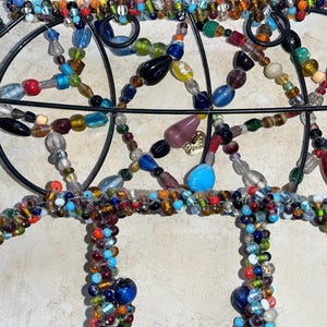 May include: Close-up of a decorative metal wall hanging adorned with colourful glass beads. The beads are in various shapes and sizes, including round, oval, and teardrop, in shades of blue, red, green, and yellow.