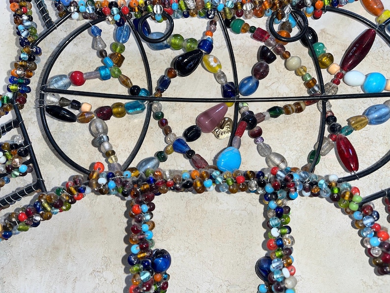 May include: Close-up of a decorative metal wall hanging adorned with colourful glass beads. The beads are in various shapes and sizes, including round, oval, and teardrop, in shades of blue, red, green, and yellow.