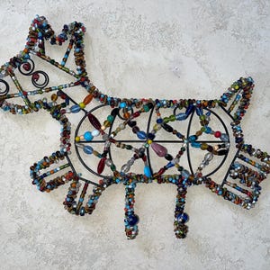 May include: A decorative dog sculpture crafted from beads and a black metal frame. The dog features a variety of colourful beads, including blue, green, red, and yellow. This handcrafted piece is designed for display.