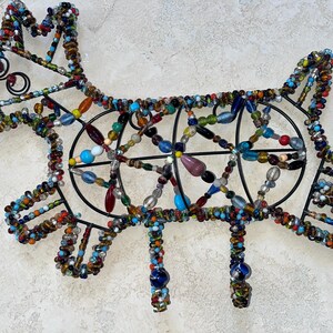 May include: A decorative dog sculpture crafted from black wire and vibrant beads. The dog's form is defined by a wire framework, embellished with an array of colourful beads. The sculpture features four legs and a tail.