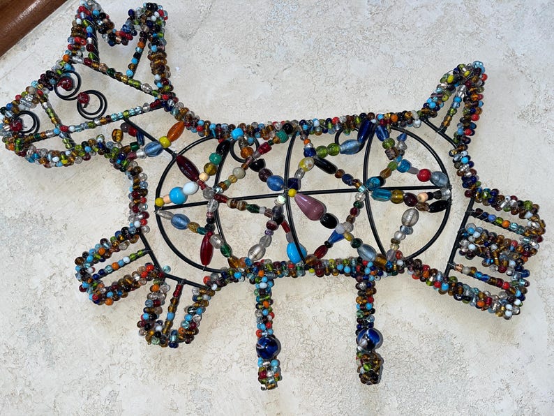 May include: A decorative dog sculpture crafted from black wire and vibrant beads. The dog's form is defined by a wire framework, embellished with an array of colourful beads. The sculpture features four legs and a tail.