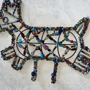 May include: A decorative metal dog silhouette, embellished with colourful beads. The dog's form is outlined in black wire, with the body and legs featuring intricate beadwork in various colours, including blue, red, and yellow.