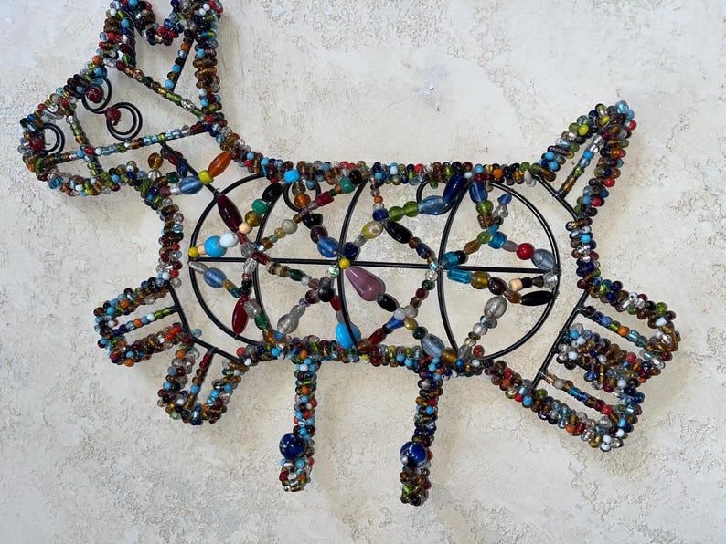 May include: A decorative metal dog silhouette, embellished with colourful beads. The dog's form is outlined in black wire, with the body and legs featuring intricate beadwork in various colours, including blue, red, and yellow.