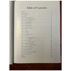 May include: Open book page with a table of contents titled "Table of Contents." The list includes chapter titles such as "Humble Beginnings," "Changing Faces," and "Barbie Footwear." The book has a pink spine.