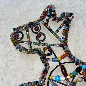May include: A decorative metal horse head silhouette, embellished with colourful glass beads. The beads are in various shapes and sizes, including round, oval, and oblong, and in shades of blue, red, yellow, and green. The horse head has a black metal frame with decorative swirls.