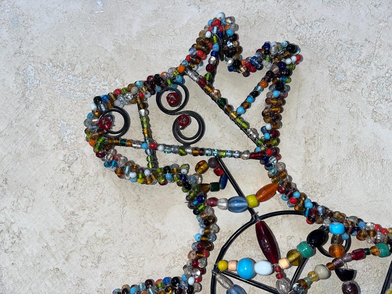 May include: A decorative metal horse head silhouette, embellished with colourful glass beads. The beads are in various shapes and sizes, including round, oval, and oblong, and in shades of blue, red, yellow, and green. The horse head has a black metal frame with decorative swirls.
