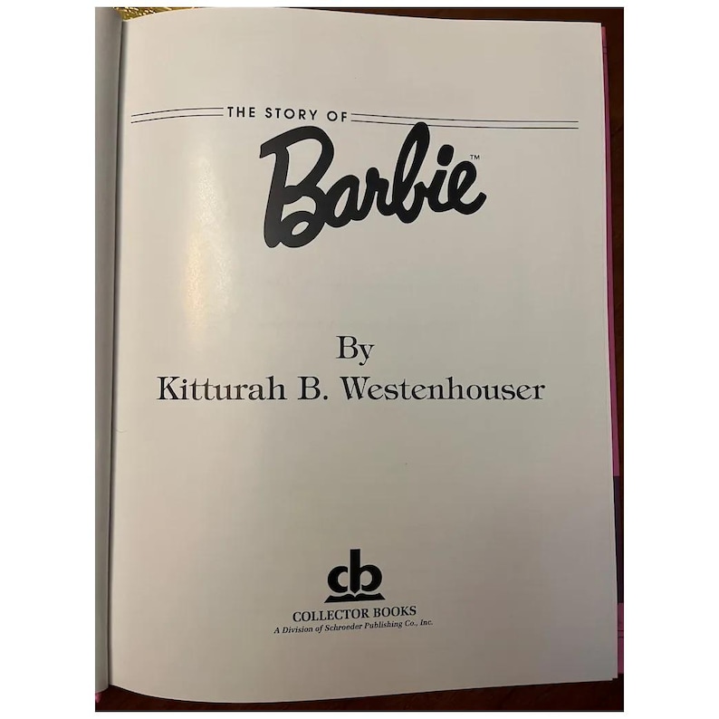 May include: Open book with a white page featuring the title "The Story of Barbie" in black script. The author's name, Kitturah B. Westenhouser, is below the title. The Collector Books logo is at the bottom.