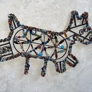 May include: A decorative dog sculpture crafted from a black metal frame and colourful beads. The beads are in various shades of blue, red, orange, and green. This unique piece of art is ideal for adding a playful touch to a home or interior space.