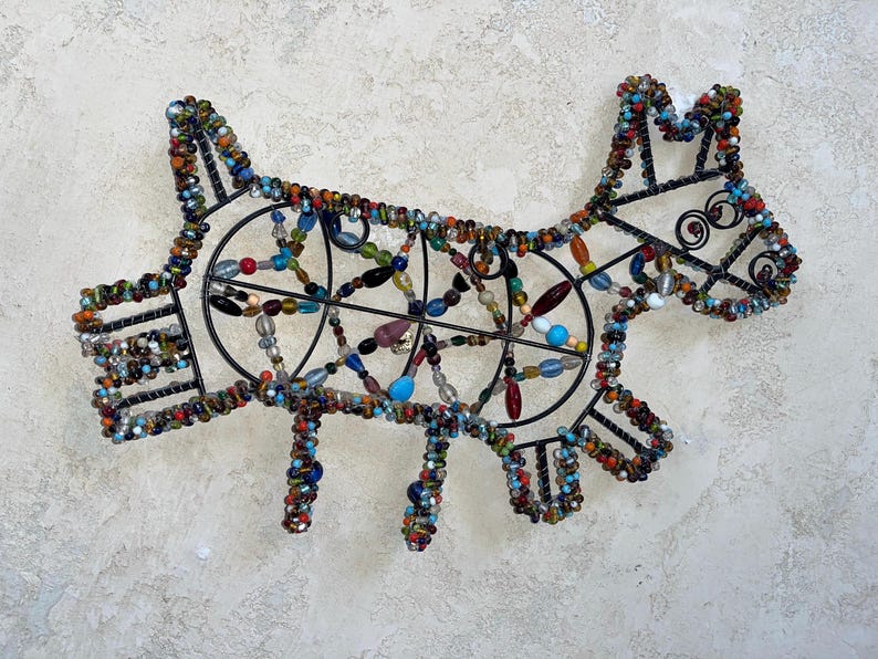 May include: A decorative dog sculpture crafted from a black metal frame and colourful beads. The beads are in various shades of blue, red, orange, and green. This unique piece of art is ideal for adding a playful touch to a home or interior space.