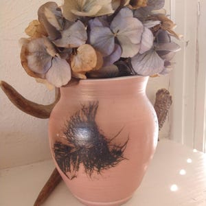 May include: A pink ceramic vase with a black abstract design, filled with dried hydrangeas.
