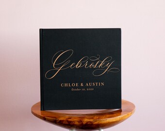 May include: A square black photo album with copper-colored foil lettering on the front cover. The text reads Gebrosky, CHLOE & AUSTIN, and October 10, 2020. The cover features a large, elegant script font for the name and simple serif text below.