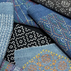 以下が含まれることがあります： 様々な刺し子刺繍パターンが施された布地の見本コレクション。青いデニムや黒い生地に、白、オレンジ、マルチカラーの幾何学的なステッチデザインが施されており、格子模様、花柄、菱形のモチーフが含まれています。