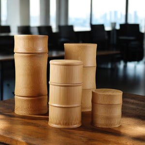 Peut inclure: Quatre contenants ronds en bambou de tailles différentes, empilés et disposés sur une surface en bois. Les contenants sont en bambou naturel de couleur brun clair.