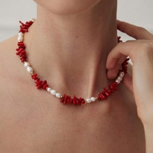 May include: A necklace with bright red coral and creamy white pearls. The necklace is strung with small gold-coloured beads, creating a striking contrast. The jewellery is displayed against a neutral background.