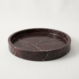 Side angle view of round burgundy marble tray showing natural veining and honed finish