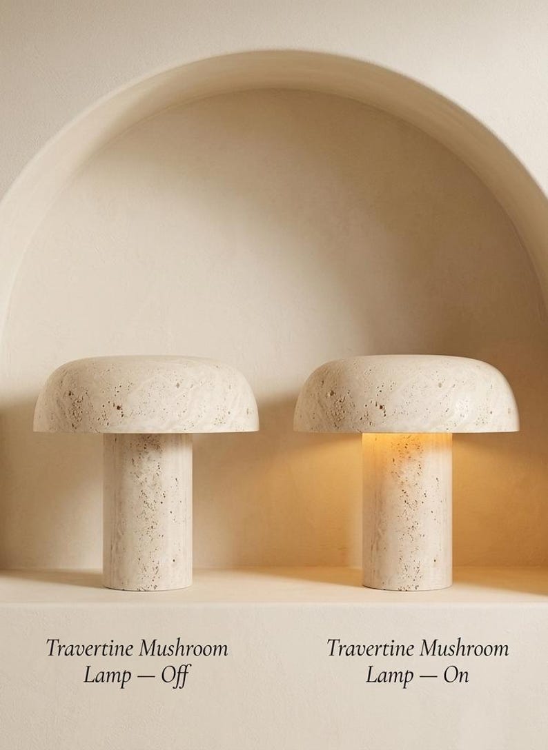 May include: Two mushroom-shaped lamps crafted from beige travertine stone with a porous, textured surface. One lamp is shown in the off position, while the other is illuminated, casting a warm glow from beneath its wide, rounded cap.
