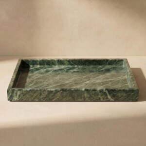 May include: A rectangular green marble tray with a polished surface. The tray has a low profile with a slightly raised edge. The marble has a natural veining pattern. Suitable for serving or display. Dimensions are approximately 30 cm x 20 cm.