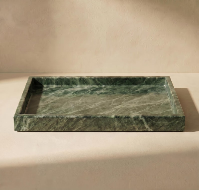 May include: A rectangular green marble tray with a polished surface. The tray has a low profile with a slightly raised edge. The marble has a natural veining pattern. Suitable for serving or display. Dimensions are approximately 30 cm x 20 cm.