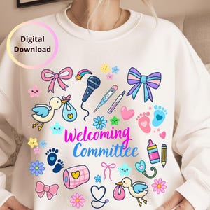 Op de afbeelding: Witte sweatshirt met kleurrijke illustraties van baby-thema-items, waaronder een ooievaar, strikken, voetafdrukken en de tekst "Welcoming Committee". De woorden "Digital Download" staan in een cirkel linksboven.