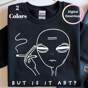 May include: Black sweatshirt with a white graphic of an alien smoking a cigarette. The text "BUT IS IT ART?" is below the alien. The words "2 Colors" and "Digital Download" are also visible.
