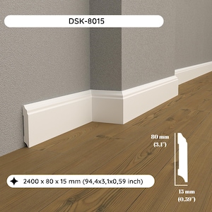 Op de afbeelding: Witte plint in een hoek gemonteerd, met afmetingen van 2400 x 80 x 15 mm. De plint staat tegen een grijze muur en een bruine houten vloer. De tekst "DSK-8015" is zichtbaar.